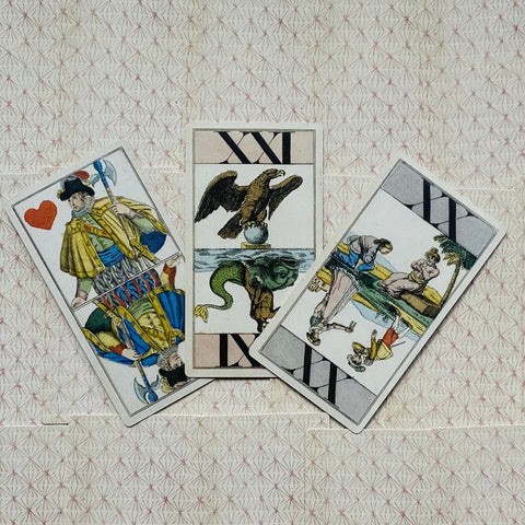 Tarot kortos trijų kortų išdėstymas: centrinė XXI su ereliu, kairė – riteris, dešinė – atversta scena ant raštuoto fono