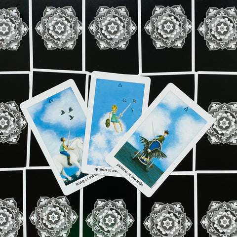 Tarot kortos – trys swords rūšies karališkos kortos su mėlyno dangaus iliustracijomis, išdėstytos ant juodo mandalos fono