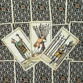tarot kortos Rider–Waite stiliaus, trys lazdų kaladžių kortos fanuotos prieš juodai‑žalią raštuotą nugarėlę
