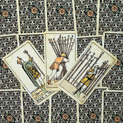 tarot kortos Rider–Waite stiliaus, trys lazdų kaladžių kortos fanuotos prieš juodai‑žalią raštuotą nugarėlę