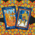 Tarot kortos, dvi mėlynais rėmais (Spider Woman ir Skadi) gretimos, rodomos priekinio kampo, ant spalvingos saulėgrąžų mozaikos fono