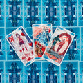Tarot kortos su iliustracijomis: trys atverstos kortos ant mėlynos simetriškos nugarėlės, fotografuota iš viršaus