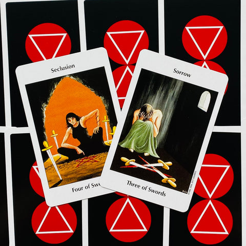 Taro kortos Rider–Waite stiliaus: dvi atvertos kortos (Four of Swords, Three of Swords), nugarėlė juoda su raudonais trikampiais