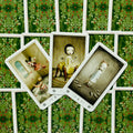 Tarot kortos — trijų kortų atversta kompozicija: centrinė figūra geltonoje suknelėje ant žalių uogotų nugarėlių