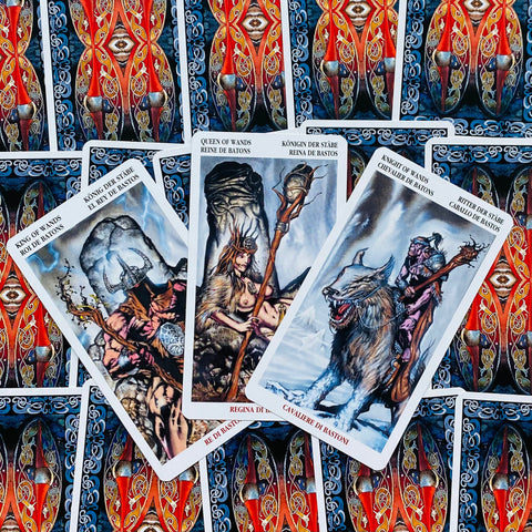 Tarot kortos Rider–Waite stiliaus, trys atverstos kortos (Karalius, Karalienė, Riteris) ant raudonai‑mėlynos ornamentuotos nugarėlės