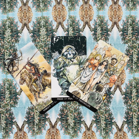 Tarot kortos fanuotos trijų kortų išdėstymas ant ornamentuoto audinio, detalūs iliustruoti personažai ir ryškios spalvos