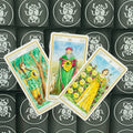 Tarot kortos – trijų Monetų rūšies kortų išdėstymas įstrižai su spalvingomis iliustracijomis ir juodomis nugarėlėmis