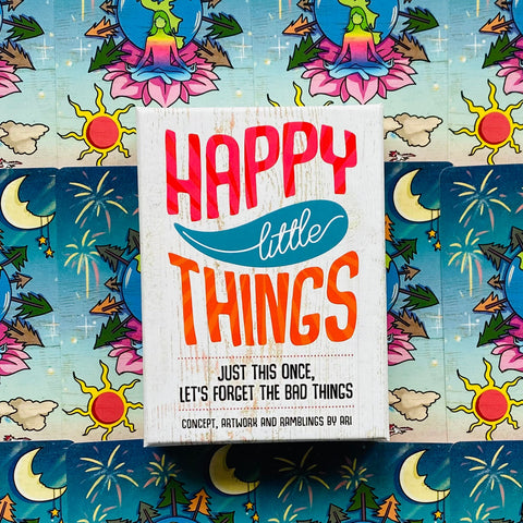kortų rinkinys Happy Little Things baltame dėkle su ryškiais užrašais, fotografuotas iš viršaus ant spalvoto raštuoto fono