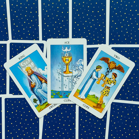 tarot kortos kompozicija: Taurių tūzas centre, Dvi taurės dešinėje, Kalavijų karalius kairėje ant mėlyno žvaigždėto fono