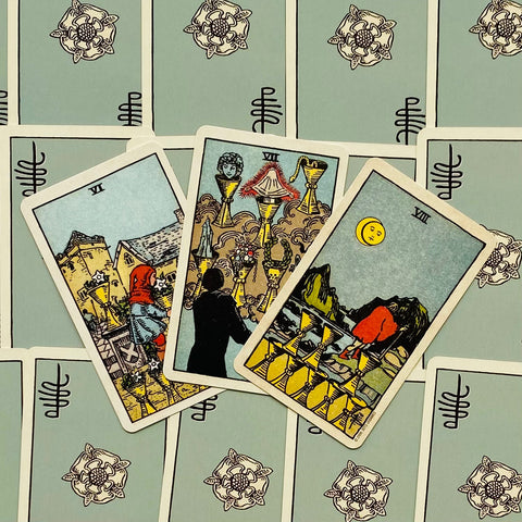 Tarot kortos Rider–Waite rinkinyje, trys taurės kortos fanuotos ant žalsvų nugarėlių, rodomas variantas iš arti