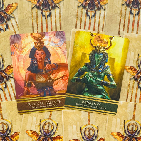 Orakulų kortos: dvi atidengtos kortos — rausvai aukso Scales of Balance ir žaliai geltona Rising Sun ant dekoratyvių nugarėlių