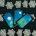 tarot kortos rinkinys — trys mėlynos taurų kortos (devyneto, aštuoneto, septynetuko) ventiliatoriumi ant juodo ornamentinio fono