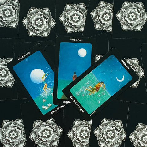 tarot kortos rinkinys — trys mėlynos taurų kortos (devyneto, aštuoneto, septynetuko) ventiliatoriumi ant juodo ornamentinio fono