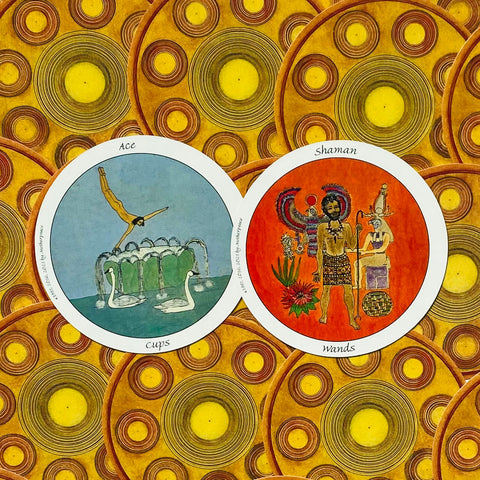 tarot kortos – dvi apvalios kortos: Ace of Cups (mėlyna) ir Shaman Wands (oranžinė) ant geltono raštuoto fono, matomos iš priekio
