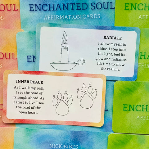 Afirmacijų kortelės Enchanted Soul Nick Bibes, spalvotos akvarelės dėžutėje, matomos Radiate ir Inner Peace kortelės su žvake ir letenų pėdomis