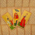 Tarot kortos su auksiniu ornamentuotu nugarėle, trys atverstos viduramžių stiliaus kortos – riteris, linksmuolis ir karalienė