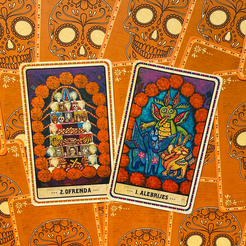 Kortos Dia de los Muertos orakulas, oranžiniai morkų marigoldai, dvi artimos kortos Alebrijes ir Ofrenda sodriomis spalvomis
