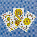 Tarot kortos su monetų rūšies raštais, trys ornamentuotos geltonos monetos išdėstytos ant mėlyno raštuoto fono