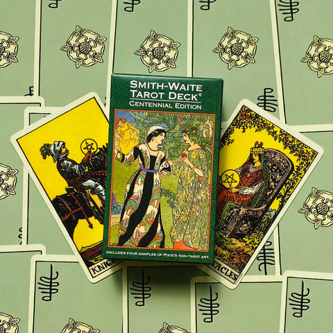 Smith‑Waite tarot kortos Centennial Edition žalia dėžutė centre, trys išskleistos pentaklių kortos fone