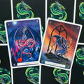 Tarot kortos su drakonų iliustracijomis — mėlyna „Love“ ir oranžinė „Mercy“ kortos parodytos iš arti, akcentuojant meninį dizainą