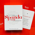 Spanda kortų rinkinys ant ryškaus raudono fono, baltos dėžutės priekis su raudonu logotipu ir matoma pavyzdinė kortelė dešinėje