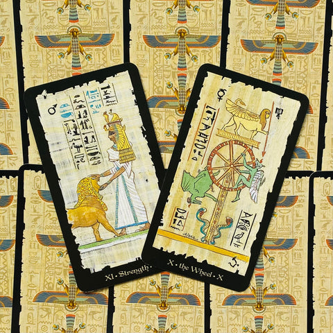 Tarot kortos egiptietiško dizaino, viršutinis kampas, dvi atverstos kortos (Stiprybė ir Ratas) ant dekoratyvios nugarėlės