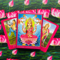 Tarot kortos Lakshmi Oracle rožinėje dėžutėje, centre matomas Lakshmi viršelis, dvi atverstos kortos šonuose ant lotoso fono