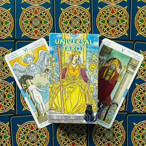 Universal Tarot geltonas dėklas su trimis didžiosios arkanos kortomis (Įsimylėję, Imperatorė, Hierofantas) ant raštuotų nugarėlių, rodoma dizaino ir spalvų variacija