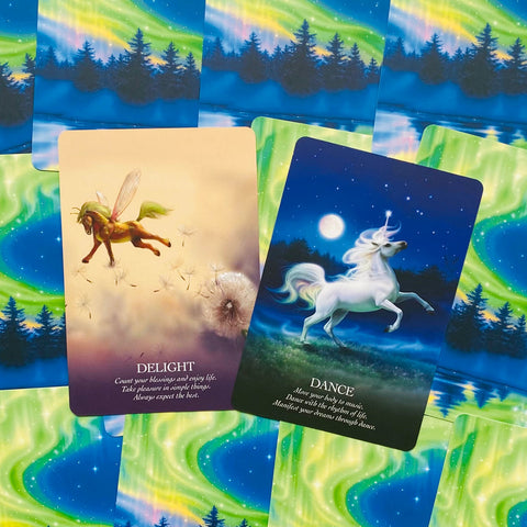 Orakulų kortos: Delight su skrendančiu arkliuku ir Dance su baltu vienaragiu, padėtos ant žaliai švytinčios auroros nugarėlės