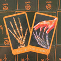 Tarot kortos su ryškiu oranžiniu rėmeliu, atverstos Ten of Swords ir Nine of Swords, vaizduojančios skeletų rankas iš viršaus