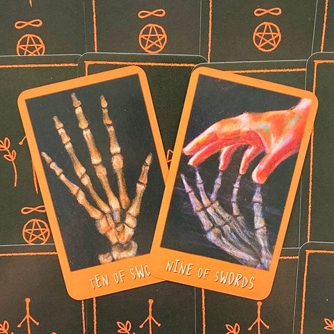 Tarot kortos su ryškiu oranžiniu rėmeliu, atverstos Ten of Swords ir Nine of Swords, vaizduojančios skeletų rankas iš viršaus