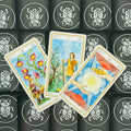 Tarot kortos trys atverstos Monetų rūšies kortos su spalvingomis akvarelinėmis iliustracijomis ant juodų vabalų nugarėlių, skirtos būrimui