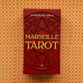 Marselio taro raudona „Professional Edition“ dėžutė (Lo Scarabeo) centre ant oranžinio raštuoto fono, matomas priekinis viršelis