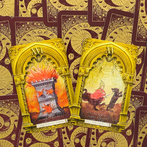Tarot kortos aukso rėmais, atvertos XVI „Degantis bokštas“ ir XV „Velnio“ kortos ant ornamentuoto bordo fono