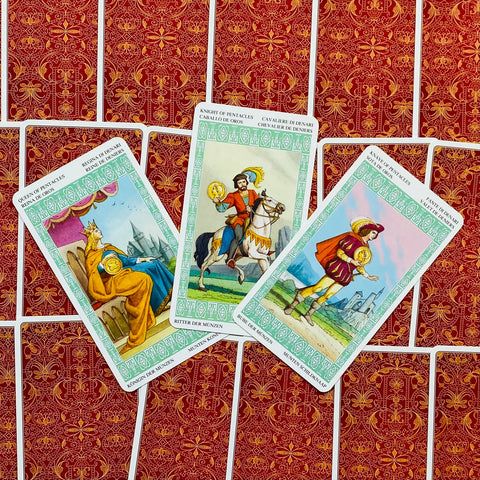 tarot kortos – atvertos trys Monetų kortos (karalienė, riteris, paštininkas) ant raudono ornamentuoto fono, rodomas kortų priekinis dizainas