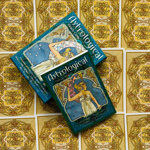 Astrologinės orakulo kortos žaliame dėkle, dvi dėžutės ant aukso raštuotų kortų nugarėlių, kampu uždėtos