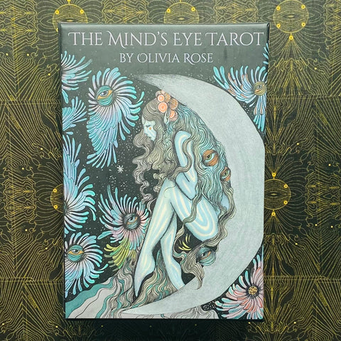 tarot kortos The Mind's Eye by Olivia Rose, mėlyno‑pilko dėklo iliustracija: sėdinti mėnulio figūra, akių motyvai ir gėlės