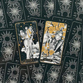 Tarot kortos juodos ir auksinės, artimas kadras su dviem atverstomis kortomis — Queen of Air ir Page of Air ant dekoratyvių nugarėlių