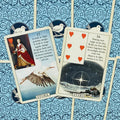 Lenormand kortos su mėlynais ornamentiniais nugarėliais, dvi atverstos kortos — Gandras ir Žvaigždės, aiškūs iliustraciniai paveikslėliai ir aiškinimai