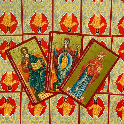 Tarot kortos su ikoniško stiliaus piešiniais, trys atverstos kortos fanuotos ant raudonai auksinio galinio rašto