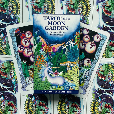 Tarot kortos Tarot of a Moon Garden dėžutė su vienaragio iliustracija, centruota ant ryškaus gėlių ir kortų fono