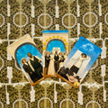 tarot kortos su suffragetė tematikos paveikslėliais, trys atviros kortos (mėlynos ir auksinės) ant ornamentuoto fono