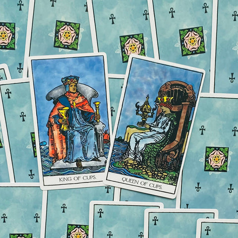 tarot kortos Rider–Waite: dvi atverstos taurų kortos (Karalius ir Karalienė) ant melsvų nugarėlių, priekinis planas
