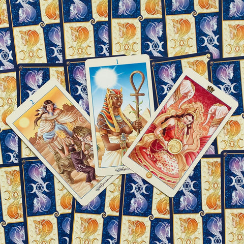 Tarot kortos su trimis atverstomis, spalvotomis iliustracijomis (Egipto moteris, karalienė, vyras) ant mėlyno‑auksinio nugarėlių