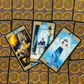 tarot kortos Rider–Waite stiliaus: trys atverstos kortos su mėlynais ženklais ir aukso rėmeliais ant ornamentuotų nugarėlių