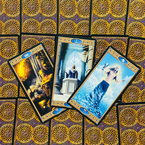 tarot kortos Rider–Waite stiliaus: trys atverstos kortos su mėlynais ženklais ir aukso rėmeliais ant ornamentuotų nugarėlių