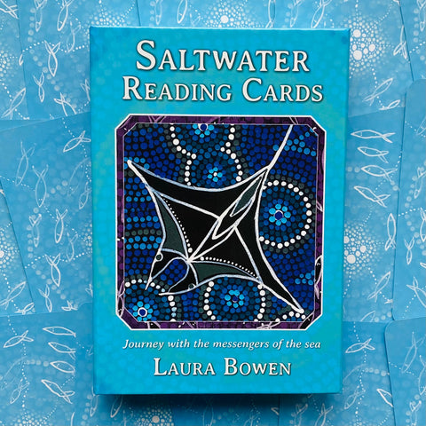 Saltwater kortos, Laura Bowen, turkio spalvos dėžutė su juodu mantos piešiniu centre ir mėlynų kortų nugarėlėmis fone, skirtos jūros tematikos skaitymams