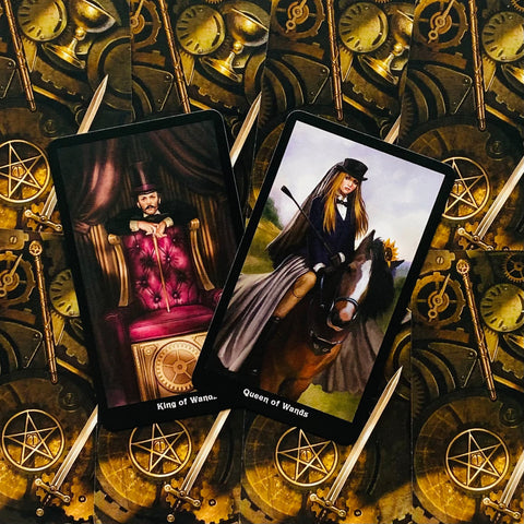 Tarot kortos su Karaliaus ir Karalienės Lazdų iliustracijomis ant auksinės mechaninių ratų nugarėlės, horizontalia kompozicija pabrėžia dizaino variantą