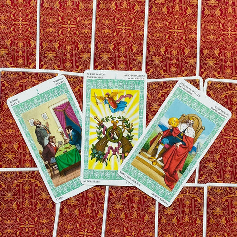 Tarot kortos Rider–Waite stiliaus žaliu rėmeliu, trijų kortų išdėstymas su Ace of Wands centre ant raudono nugarėlių rašto