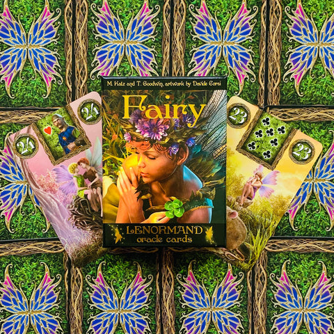 Lenormand orakulo kortos Fairy: spalvinga dėžutė centre ir trys išskleistos kortos ant žalsvo, drugelių raštuoto fono